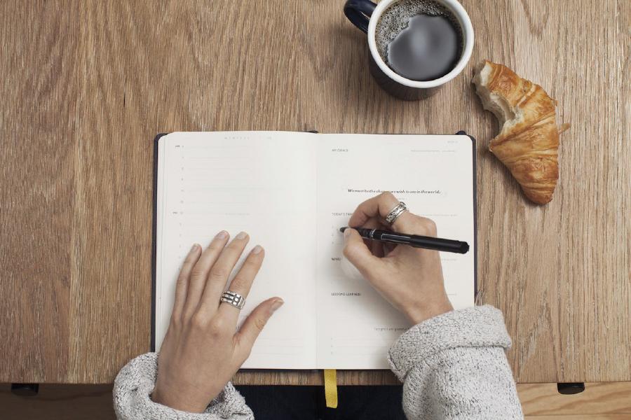 Hands writing priorities in a notebook during planning